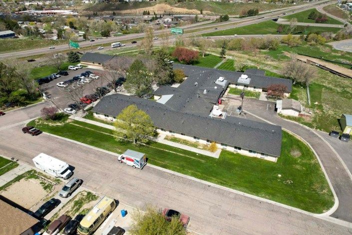 Aerial view of a residential building with surrounding greenery and parking area.