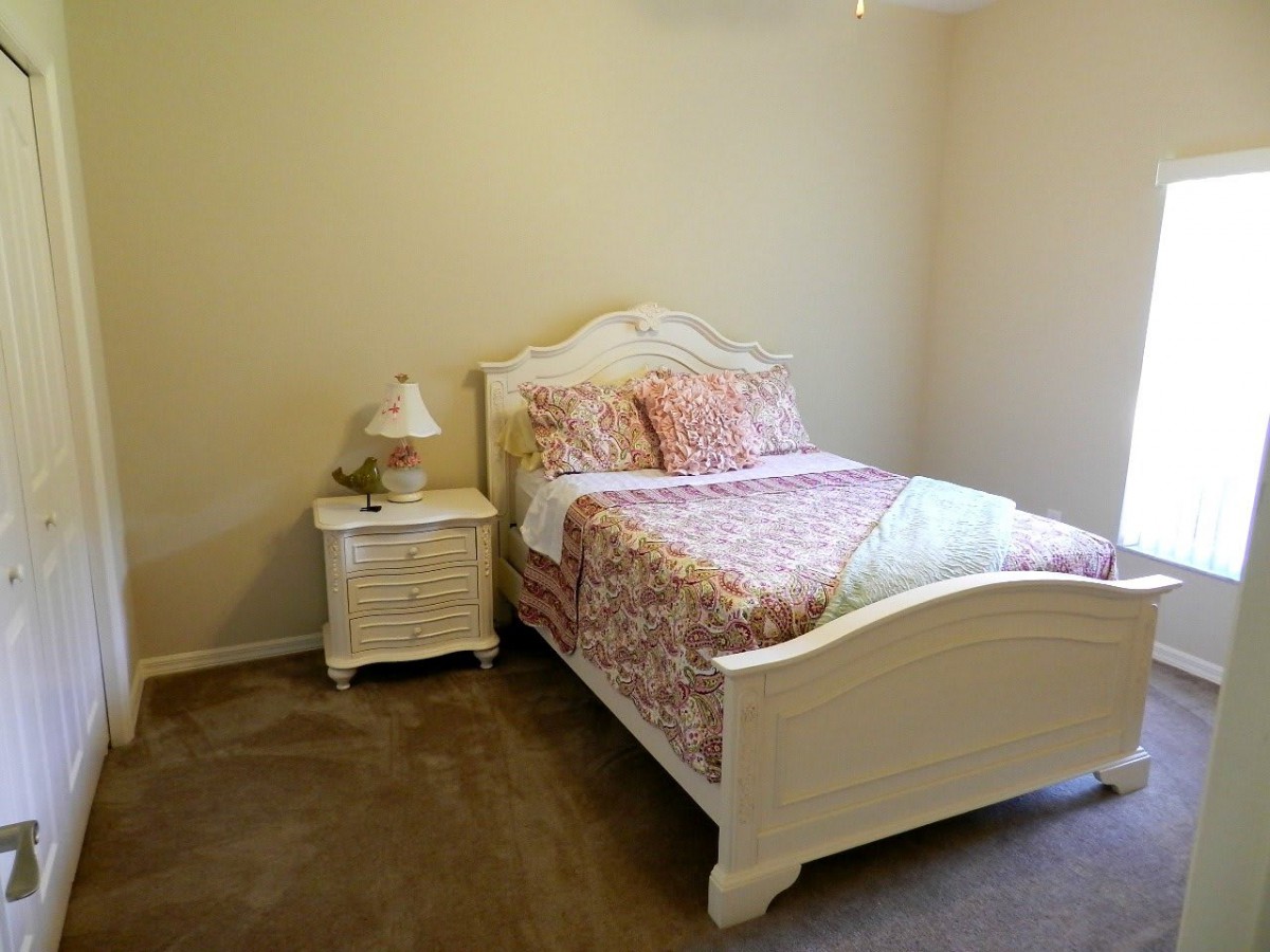 A cozy bedroom with a white bed, floral bedding, and a matching nightstand with a lamp.