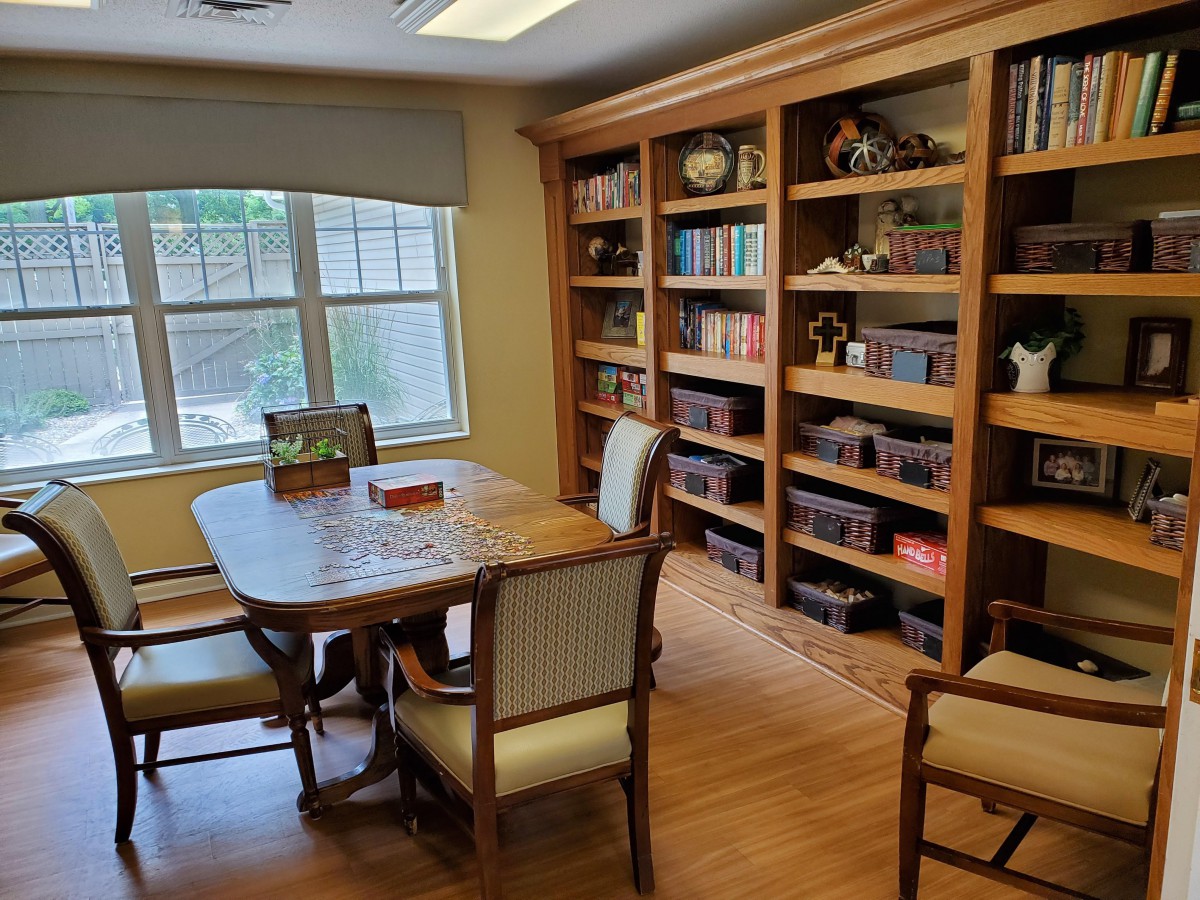 A cozy library room with wooden bookshelves, a table, and chairs by the window.