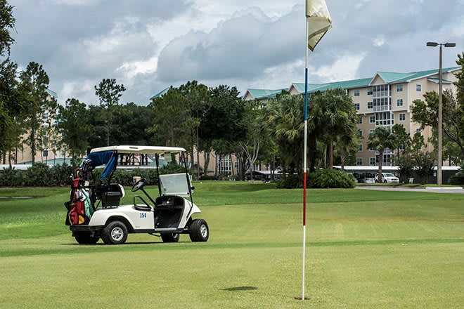 A golf cart parked on the green beside a flag on a cloudy day.