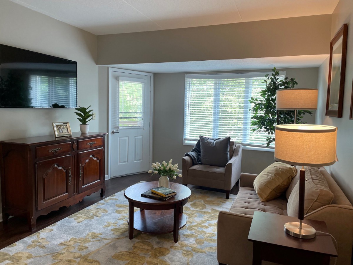 A cozy living room with a comfortable seating area, a television, and natural lighting from a large window.