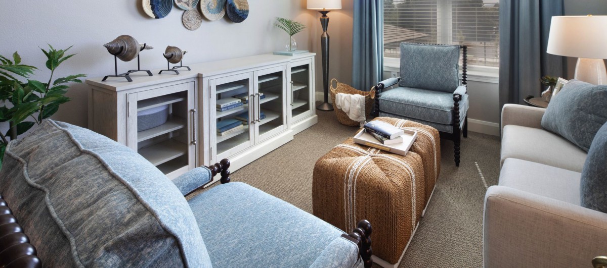 A cozy living room featuring blue chairs, a patterned ottoman, a white cabinet, and elegant decor.