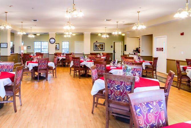 A well-lit dining room with neatly arranged tables and chairs, featuring elegant chandeliers and a wooden floor.