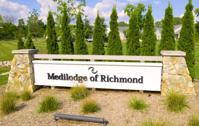 A sign for Medilodge of Richmond surrounded by trees and landscaping.