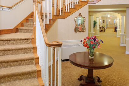 A welcoming entryway featuring a staircase, decorative mirror, and a round table adorned with a bouquet of flowers.