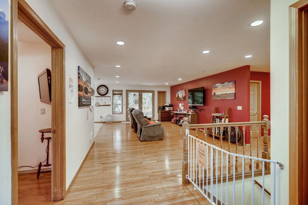 A spacious living room featuring hardwood floors, comfortable seating, a television, and a red accent wall, with a view of the staircase.