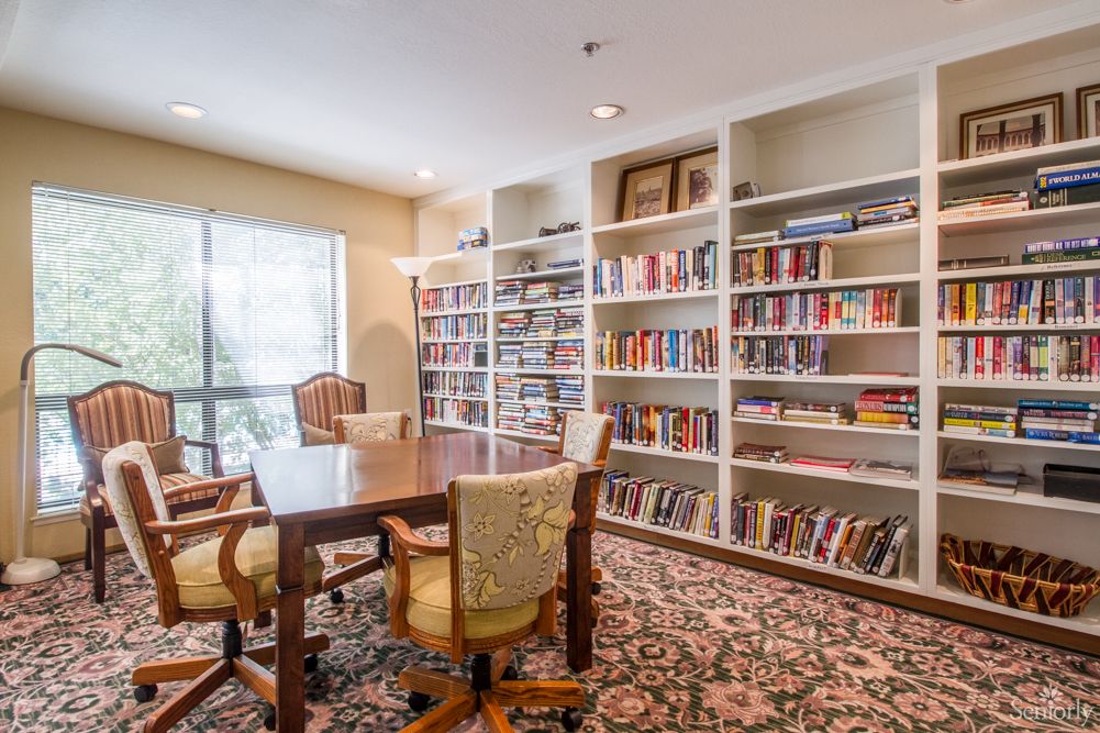 A cozy library room with bookshelves filled with books and a table surrounded by chairs.