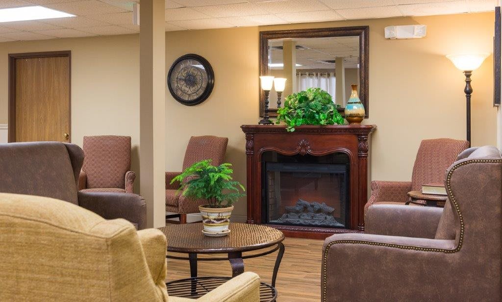 A cozy living room with a fireplace, comfortable chairs, and green plants.