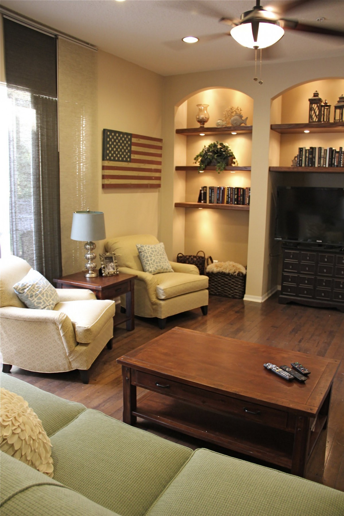 A cozy living room with armchairs and a wooden coffee table, featuring shelves with books and a flag decoration.