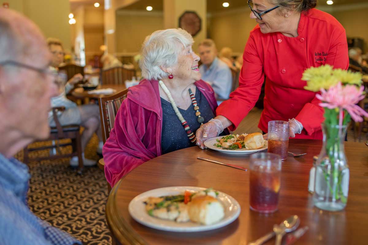 An elderly woman is being served a meal by a server in a restaurant setting.