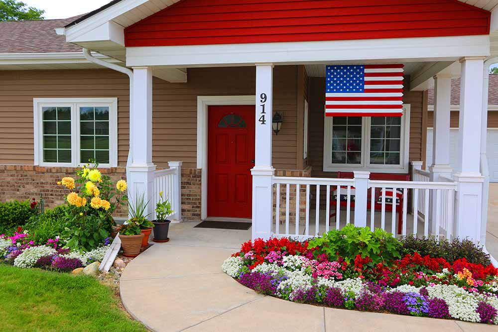 A cozy house with a red door, an American flag, and a beautifully landscaped garden.