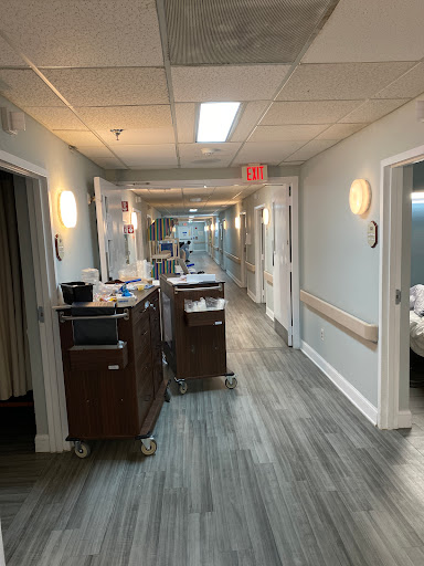 A well-lit hallway in a medical facility, featuring patient rooms and healthcare equipment.