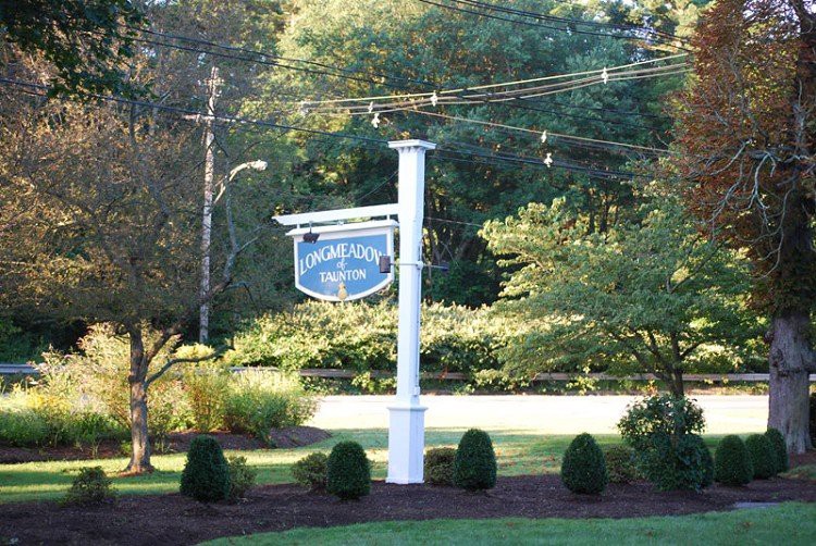 A signpost in a landscaped area with trees and shrubs in the background.