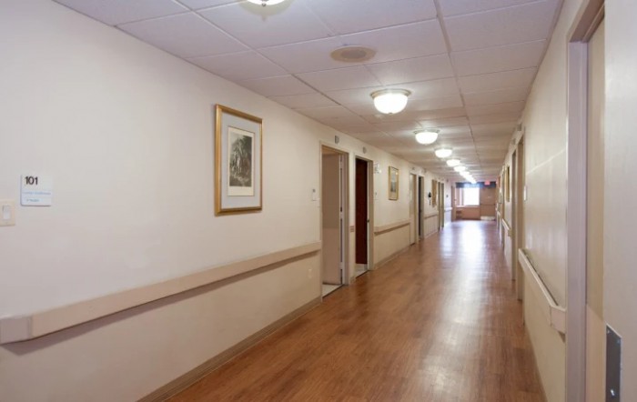 A long indoor hallway with a wooden floor and ceiling lights, adorned with framed pictures on the walls.