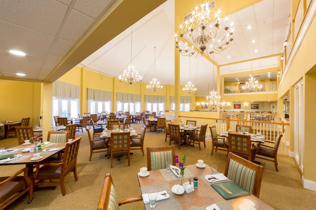 An elegant dining room with chandeliers, decorated in a warm color palette, featuring neatly arranged tables and chairs.