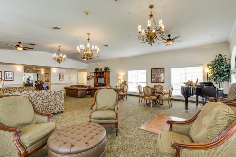 A spacious and elegantly decorated living area with comfortable seating, chandeliers, and a piano, perfect for social gatherings.