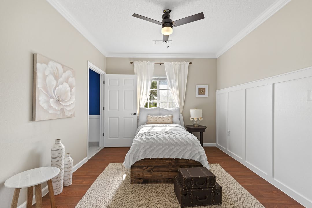 A cozy bedroom featuring a single bed, ceiling fan, and neutral decor.