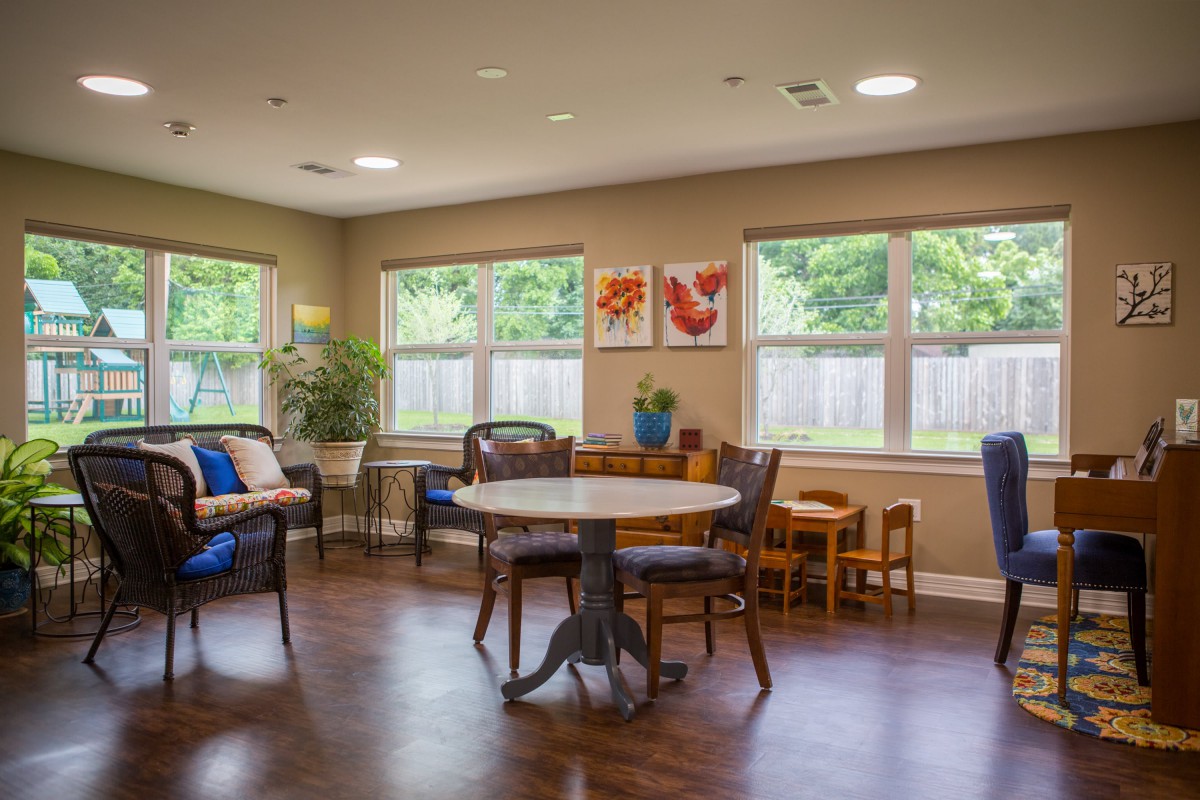 A cozy living room with large windows, featuring a round table and chairs on a wooden floor.