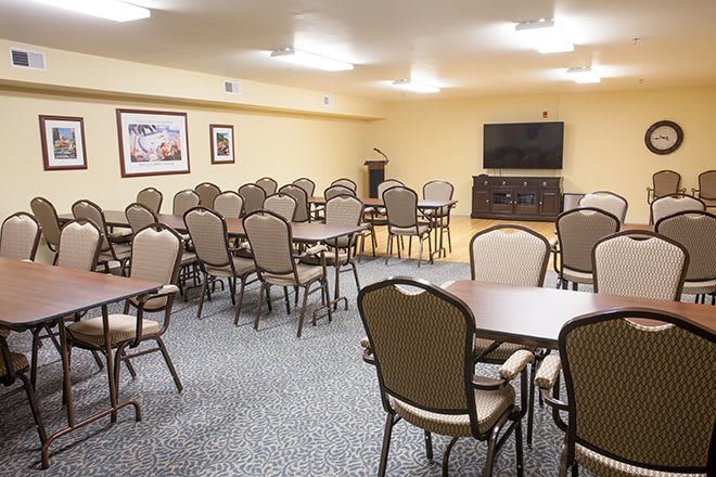 A conference room with multiple tables and chairs, featuring a TV and carpeted floor.