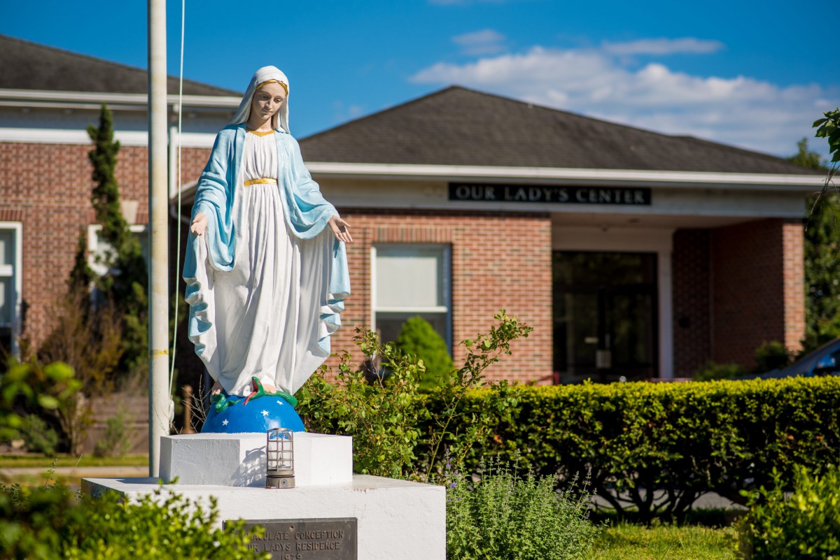 A statue of the Virgin Mary in front of a brick building under a blue sky.