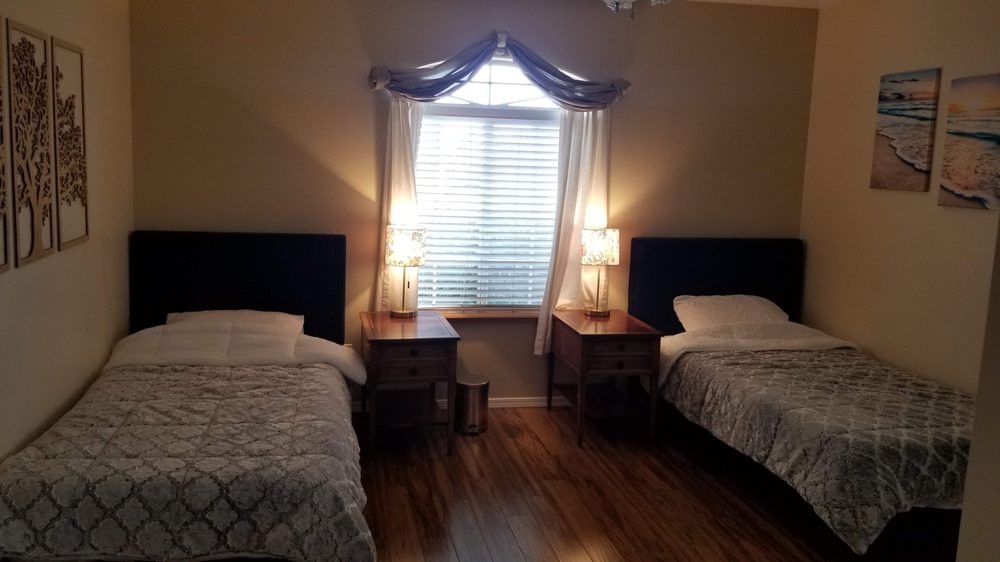 A cozy bedroom with two twin beds, nightstands, and lamps, featuring a window with curtains.