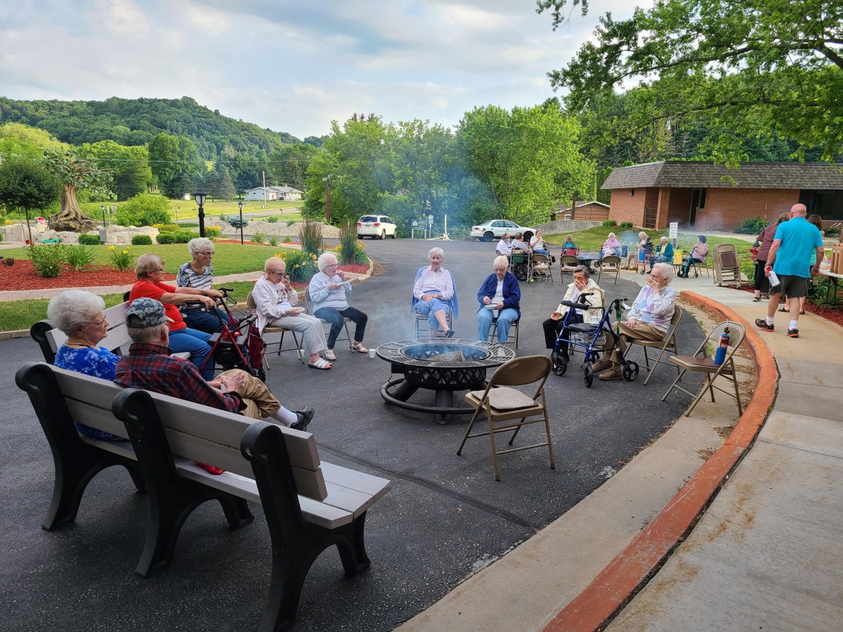 A group of people sitting around a fire pit outdoors with a scenic backdrop.