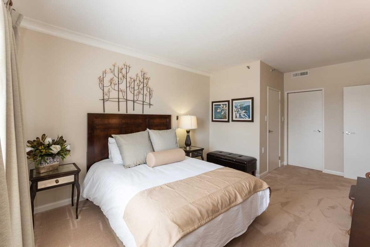 A cozy bedroom with a neatly made bed, decorative pillows, wall art, and a bedside lamp.