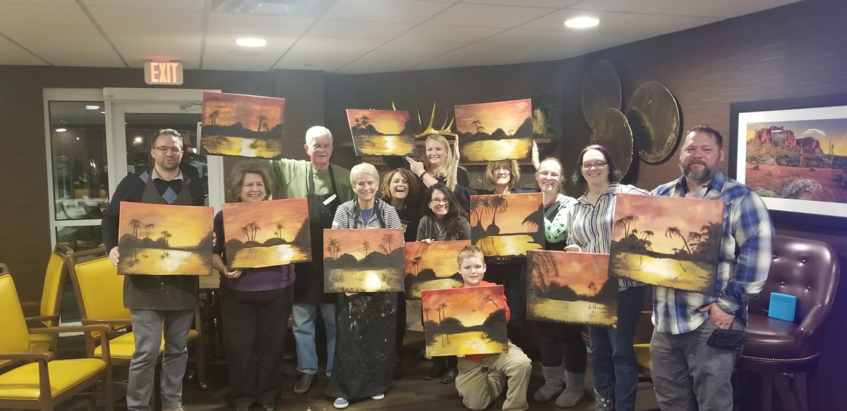 A group of people proudly displaying their completed paintings in an art class setting.