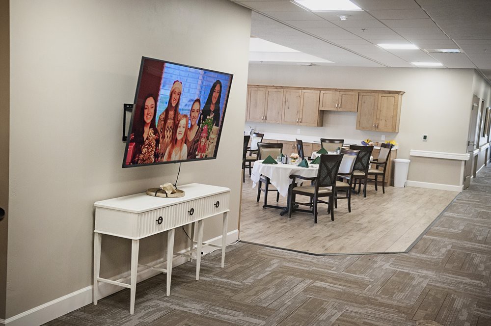 A modern living space featuring a wall-mounted television and a dining area in the background.