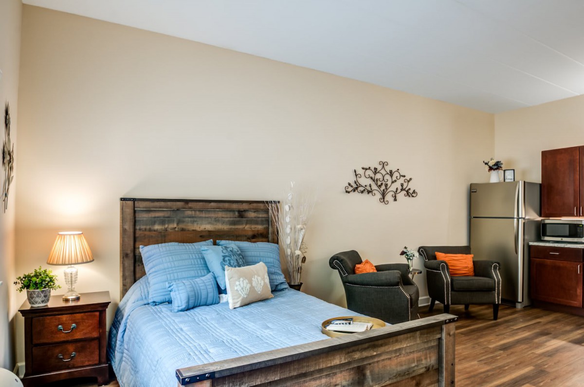 A cozy bedroom with a wooden bed frame, blue bedding, and comfortable seating area.