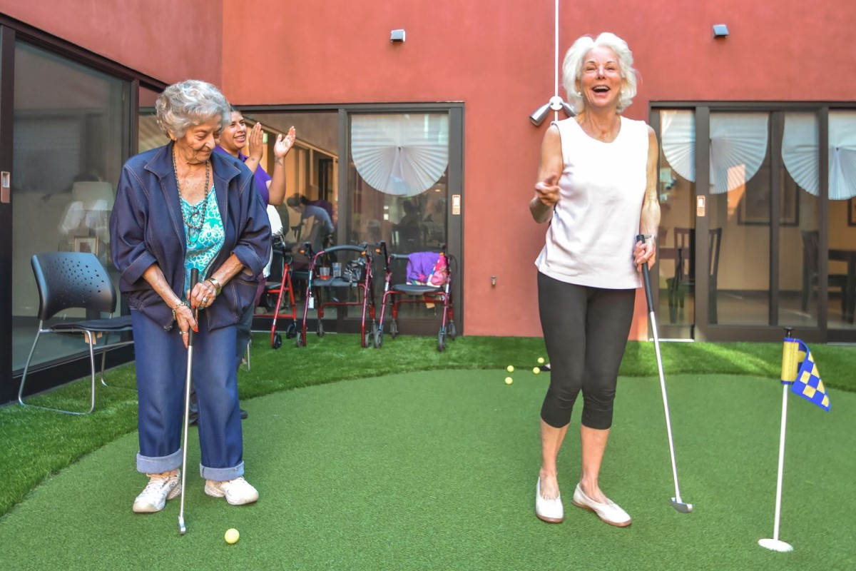 Two seniors enjoying a game of mini-golf outside.
