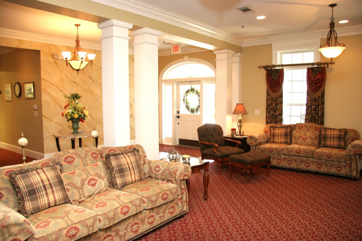 A cozy living room with elegant furniture and classic decor, featuring sofas, armchairs, and a chandelier.