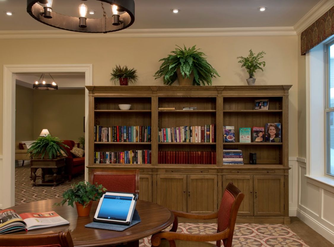 A cozy library with bookshelves, a table with a laptop, and comfortable seating.