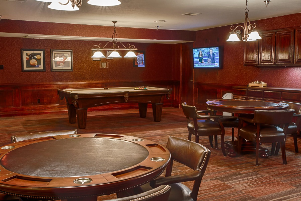 A cozy game room featuring a pool table, poker tables, and wooden interiors.