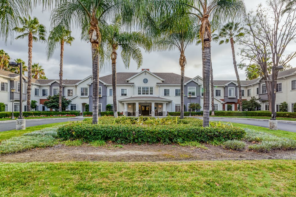 A large building with a grand entrance surrounded by palm trees and greenery under a cloudy sky.