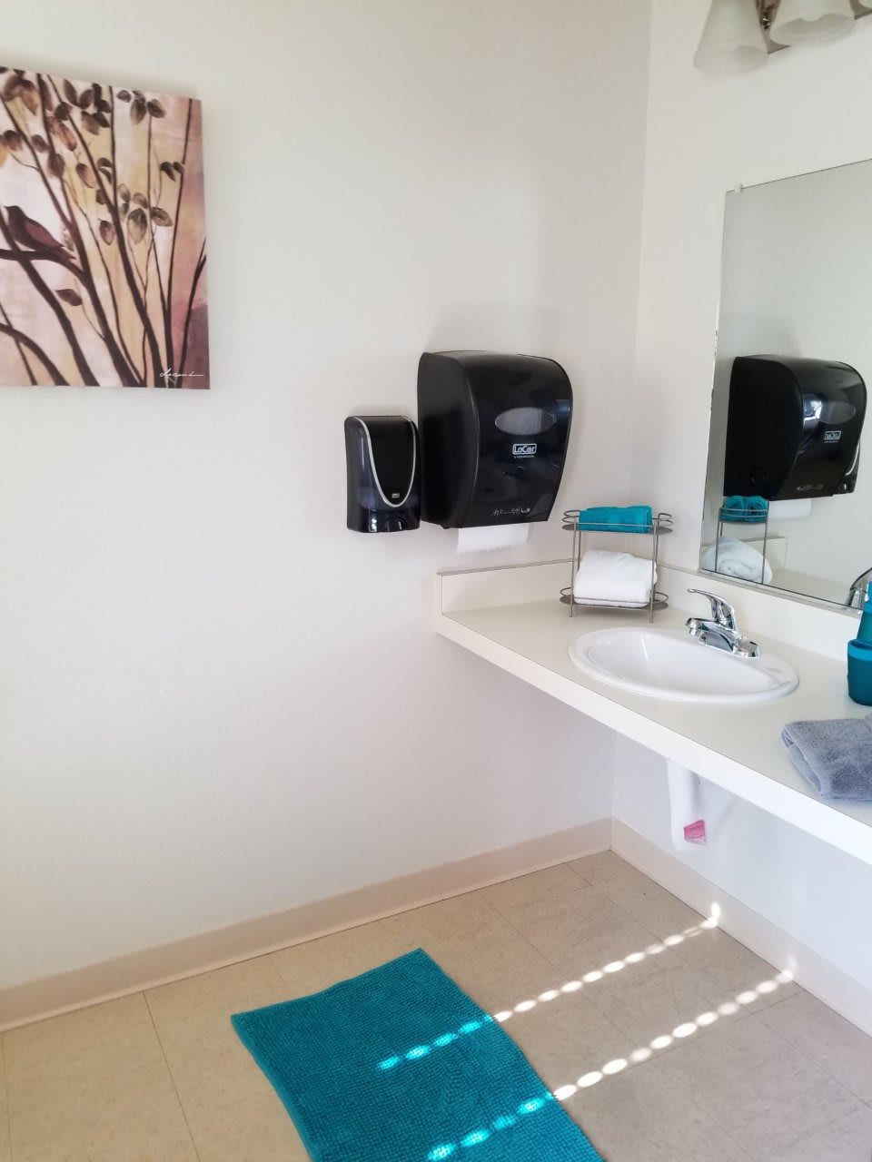 A clean and modern bathroom with a sink, mirror, and wall-mounted soap dispenser.