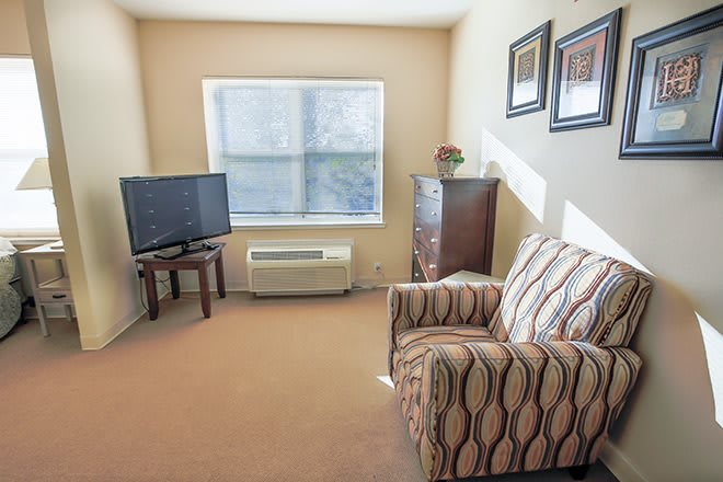 A cozy living room with a striped armchair, television, and window letting in natural light.