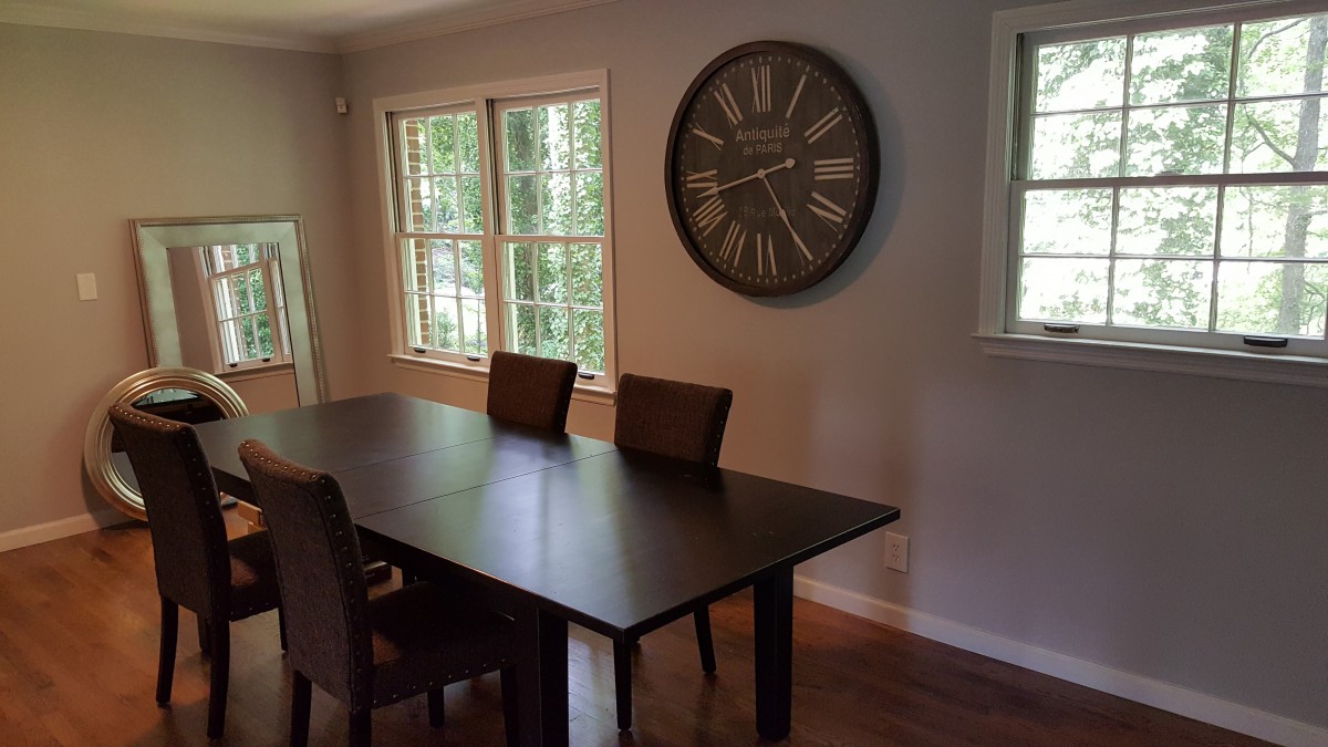 A dining room with a wooden table, chairs, and a large wall clock.
