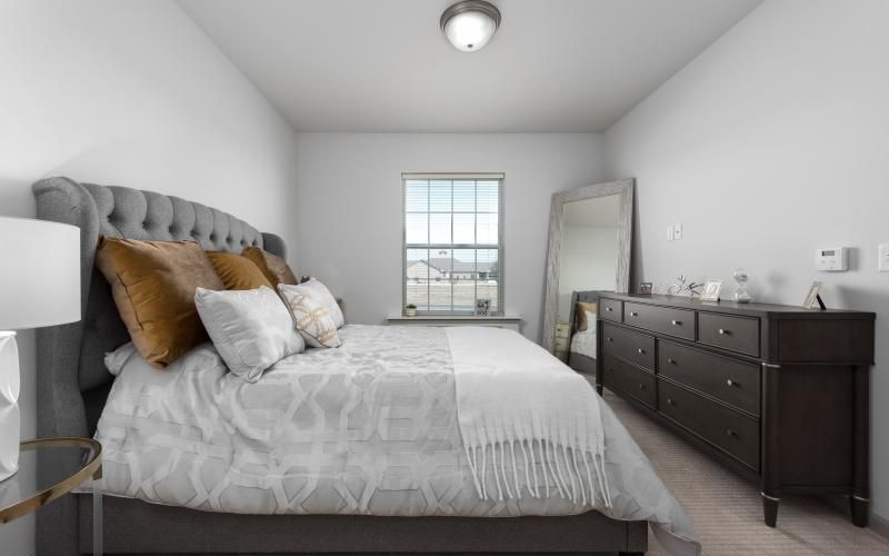 A modern bedroom with a neatly made bed, large dresser, and standing mirror.