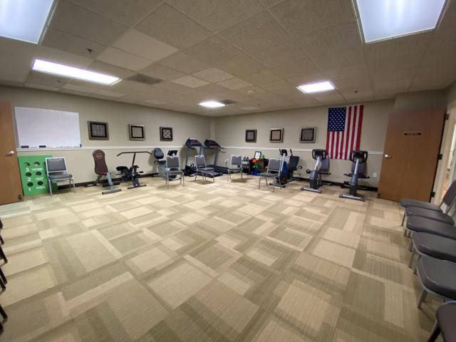 A small exercise room with stationary bikes and treadmills, featuring an American flag on the wall.