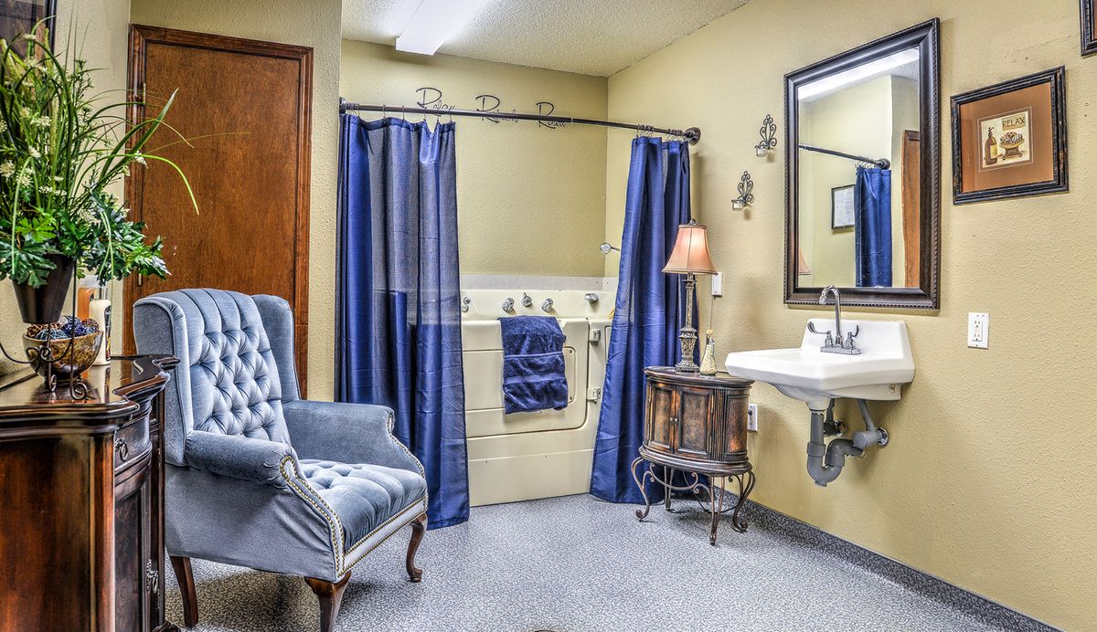 A cozy bathroom featuring a bathtub with blue curtains, a sink with a mirror above, and an upholstered chair.