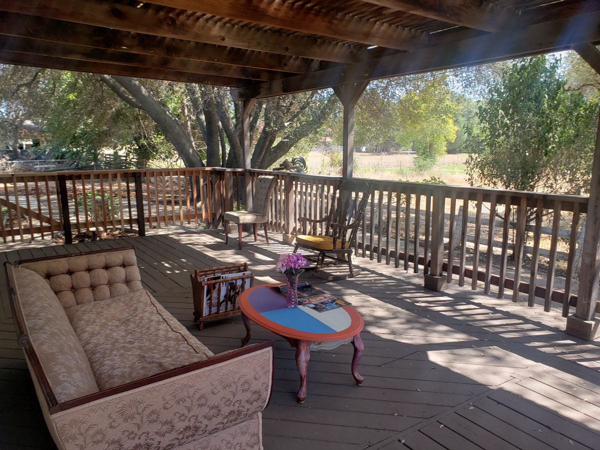 A cozy outdoor patio with wooden furniture, shaded by trees.