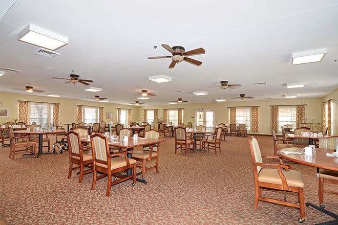 A spacious dining area with wooden tables and chairs, ceiling fans, and multiple windows.