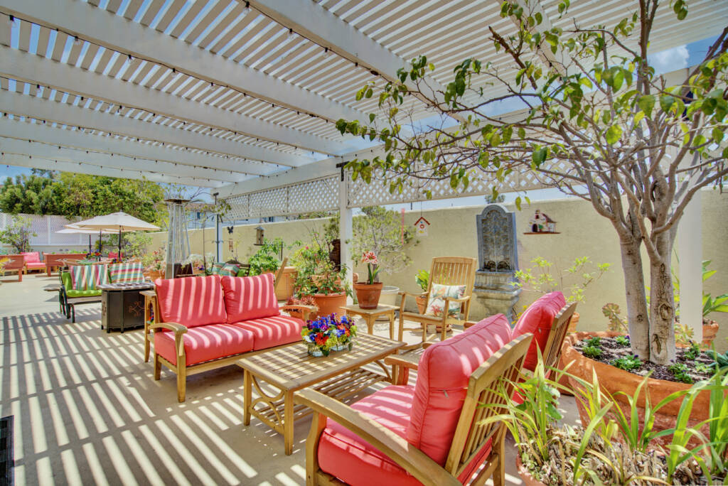 A cozy outdoor patio with colorful seating under a pergola, surrounded by lush greenery.