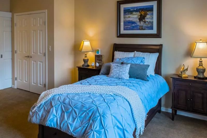 A cozy bedroom with a blue-themed bed and a nightstand lamp.