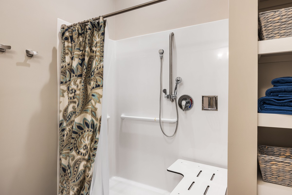 A bathroom with an accessible shower featuring a floral curtain and a built-in shower seat.