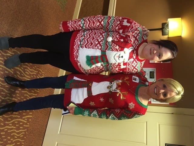 Two people wearing festive Christmas sweaters indoors.