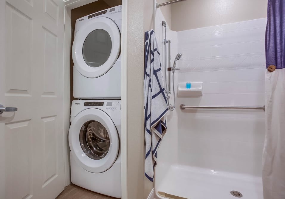 A bathroom with a stacked washer and dryer unit next to a shower.