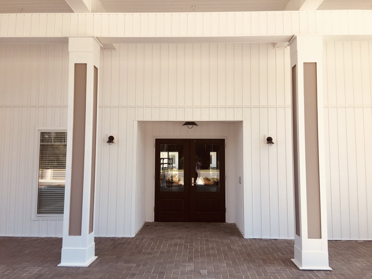 A modern building entrance with a white exterior and columns flanking a dark wooden door.
