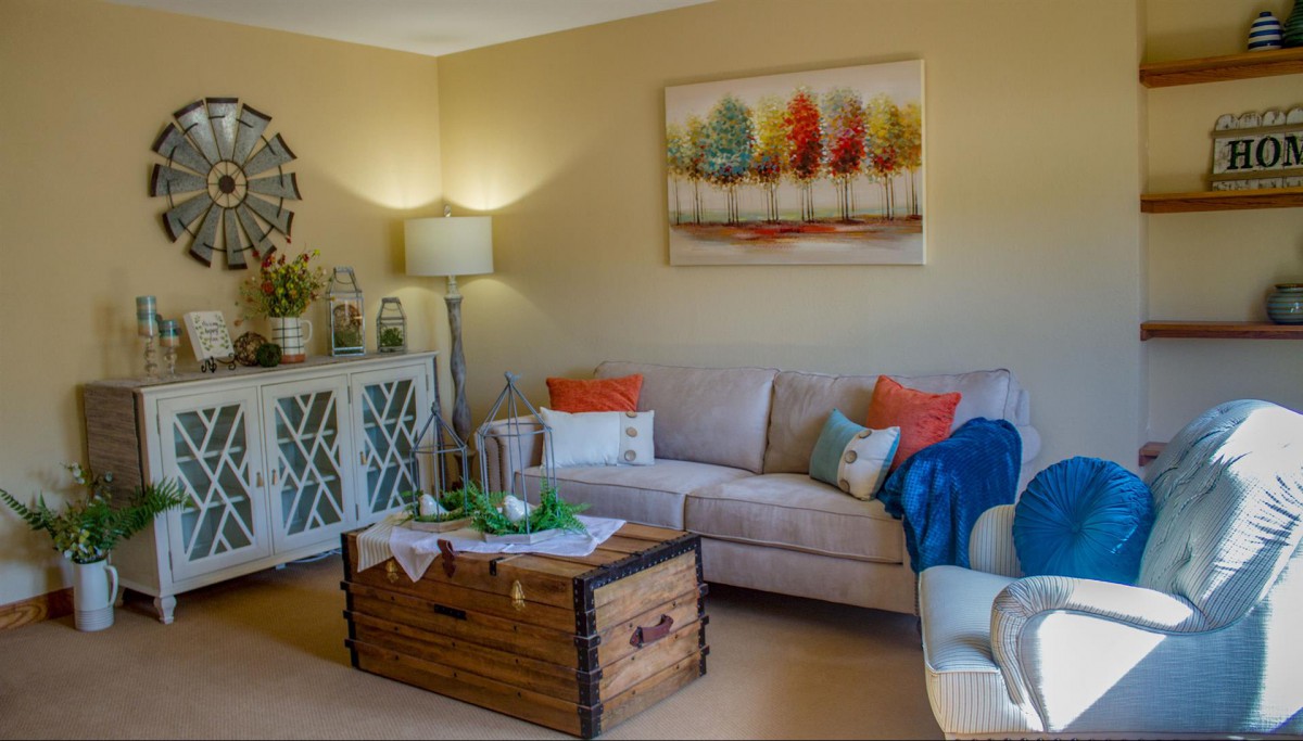 A cozy living room with a sofa, colorful pillows, a wooden coffee table, and artistic wall decor.